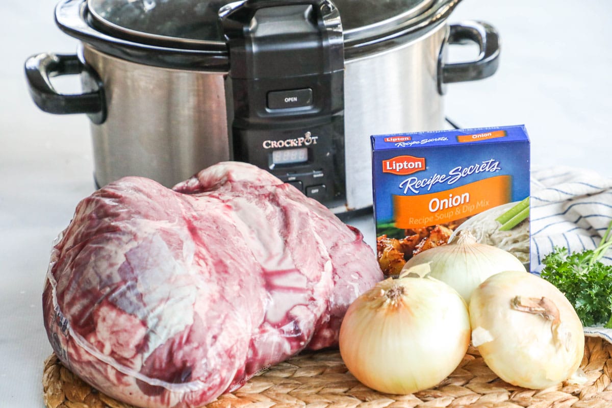 Slow cooker and ingredients for making sirloin tip roast, including meat, onions, and onion soup