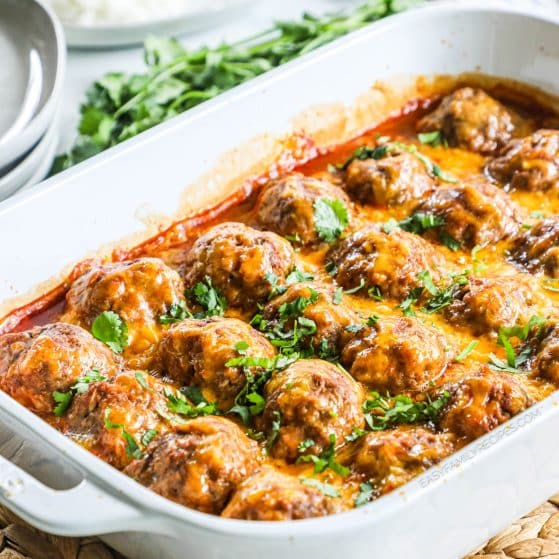 Casserole dish with meatballs in enchilada sauce and melted cheese on top.