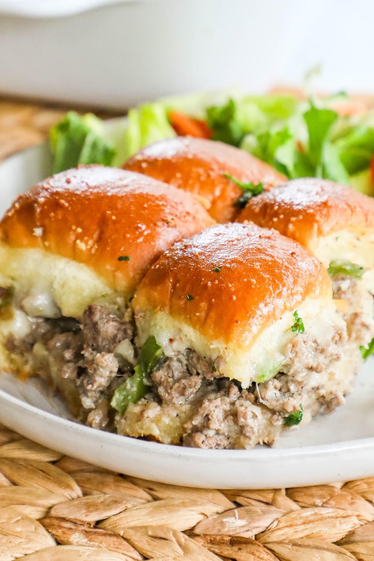 Philly Cheesesteak sliders with ground beef filling on Hawaiian rolls on a plate with salad