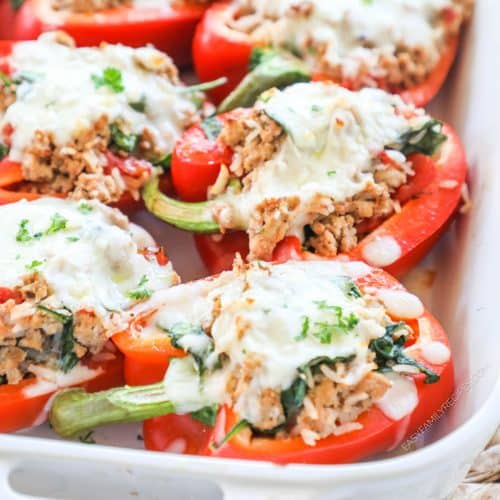 Ground chicken stuffed peppers topped with cheese in baking dish