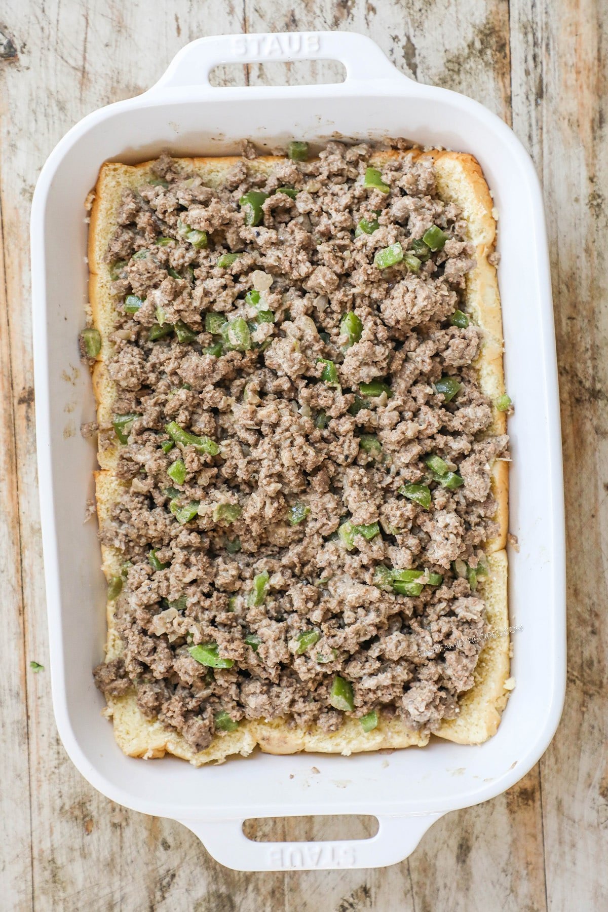 How to make philly cheesesteak sliders - step 3 - Cut the slider rolls in half horizontally and lay the bottom sections in a 9×13 baking dish. Spread the beef mixture evenly over the rolls.