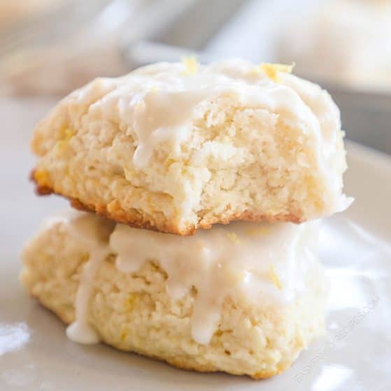 Two glazed lemon scones stack on top of each other with a bite taken out of the top one.