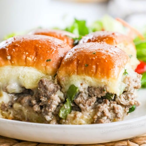 Philly Cheesesteak sliders with ground beef filling on Hawaiian rolls on a plate with salad