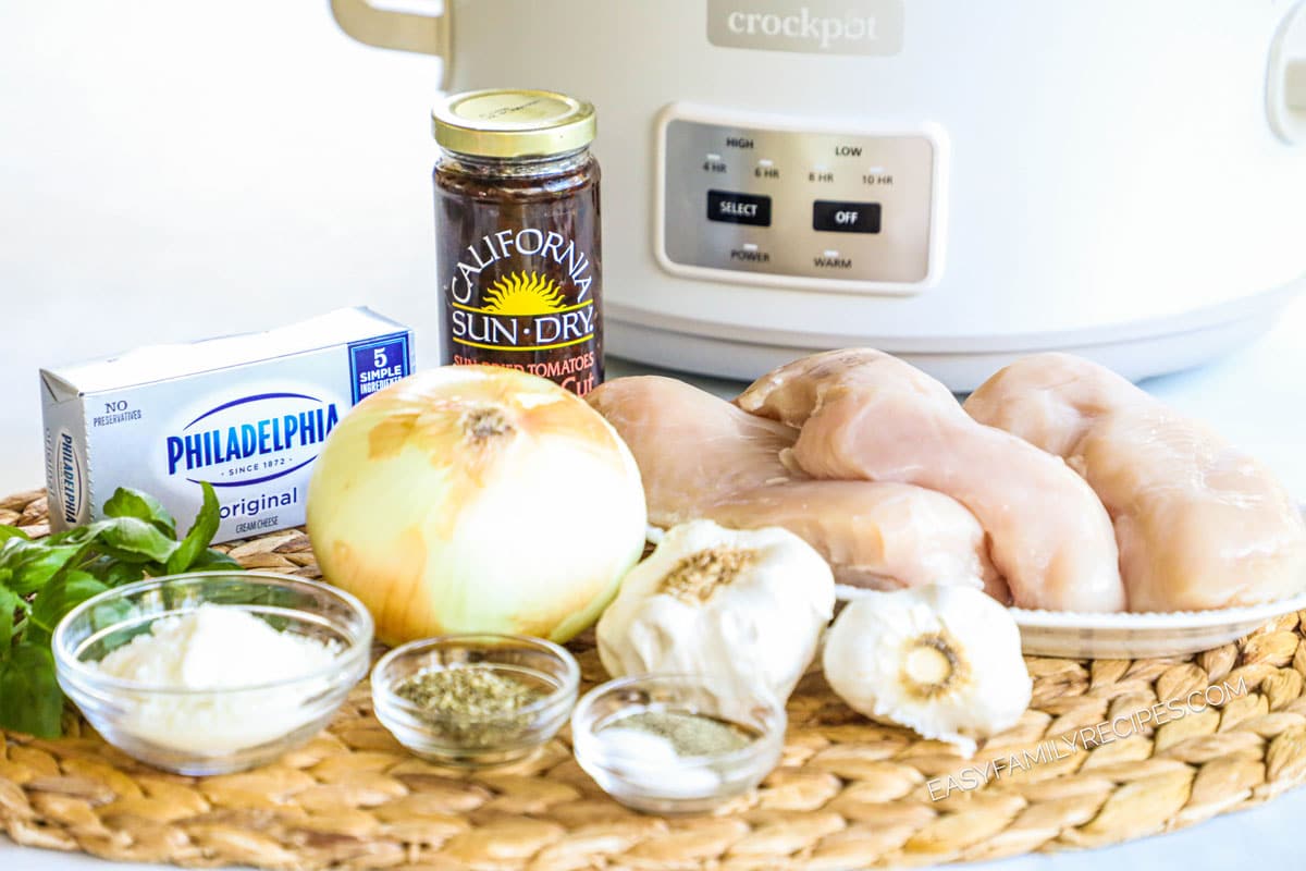 Ingredients for crockpot marry me chicken, including chicken breasts, cream cheese, sun-dried tomatoes, garlic onions, and basil