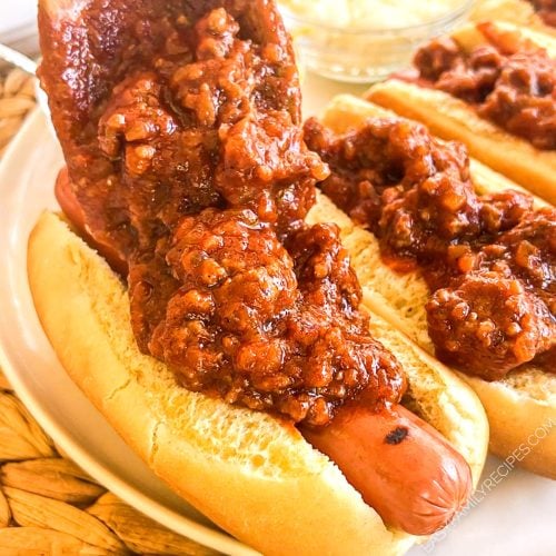 A spoon ladling chili over a hot dog in a bun.