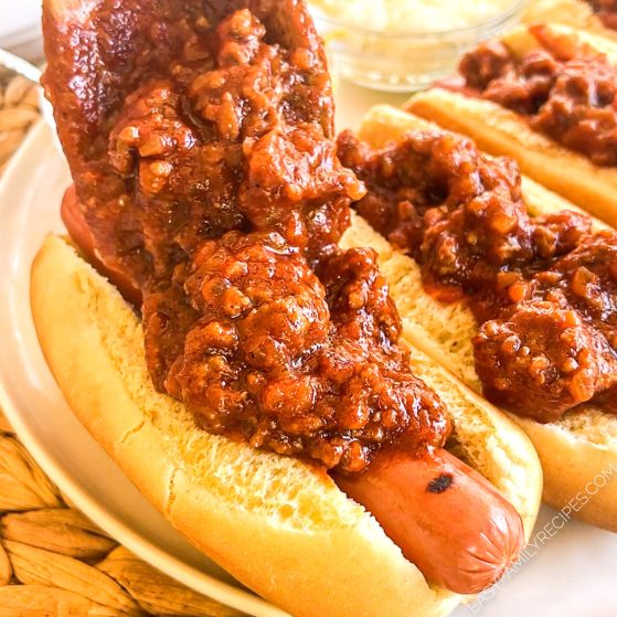 A spoon ladling chili over a hot dog in a bun.