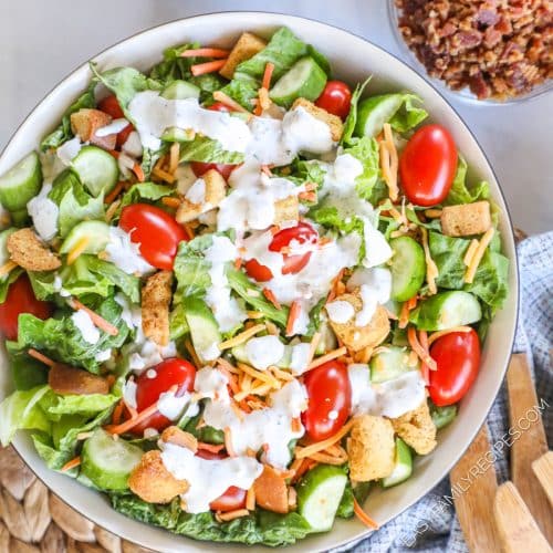 Prepared house salad with romaine lettuce, tomatoes, cucumber, cheese, and buttermilk ranch dressing