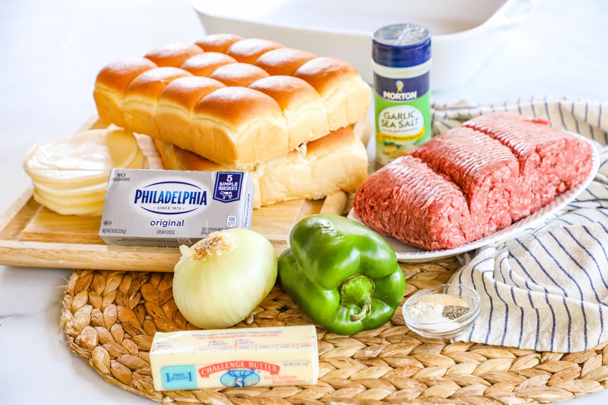 ingredients to make philly cheesesteak sliders including Hawaiian slider rolls, cream cheese, butter, onions, green bell peppers, ground beef and seasonings