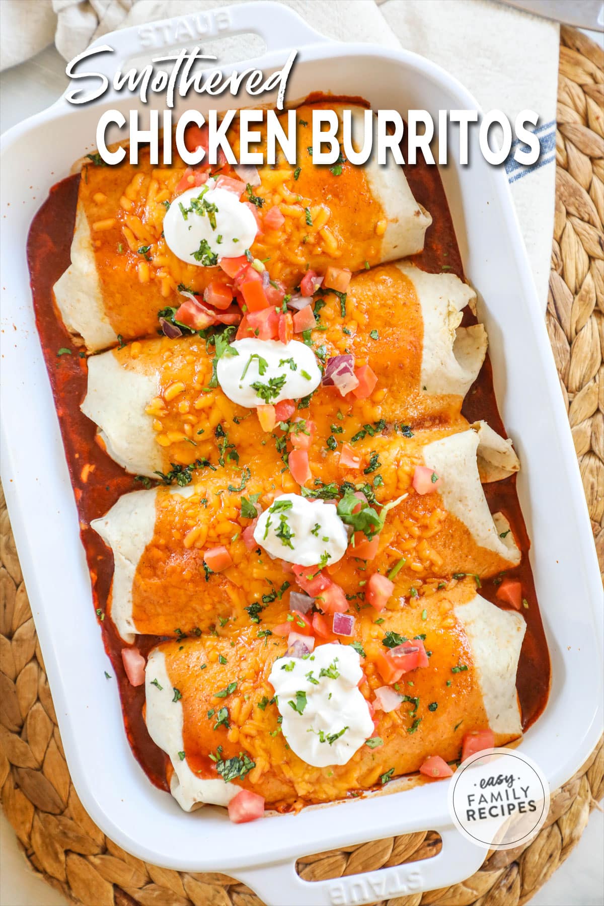 a pan of smothered burritos topped with cilantro, sour cream, and pico de gallo.