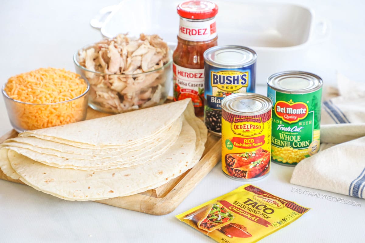 Ingredients to make smothered shredded chicken burritos including flour tortillas, corn, beans, enchilada sauce, salsa, and cheese.