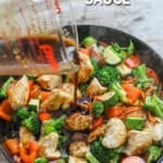 Pouring stir fry sauce into chicken and vegetables to prepare dinner.