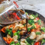 Stir Fry sauce recipe being poured over chicken and vegetables in hot pan.