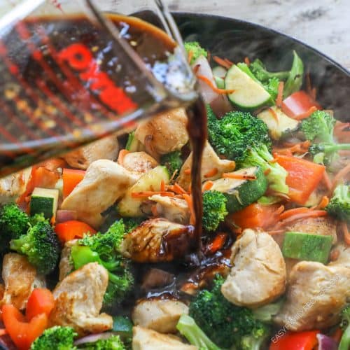 Pouring stir fry sauce on to chicken and vegetables