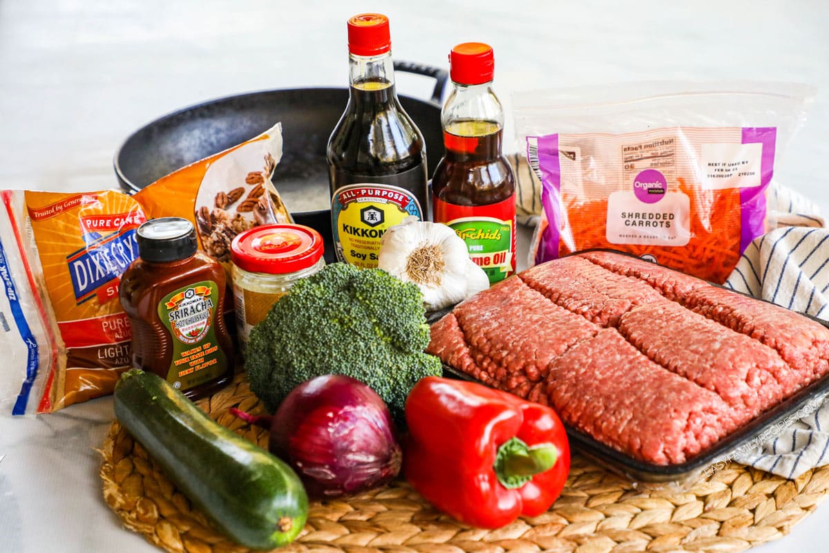 Ingredients to make ground beef stir fry with vegetables including peppers, zucchini, broccoli, onion, and carrots.