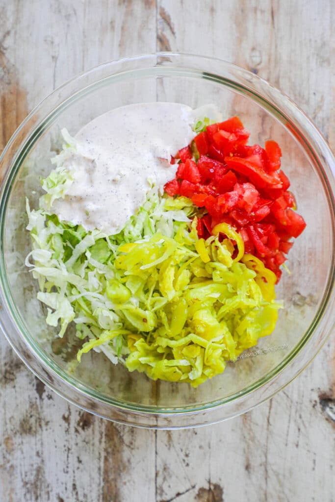 How to make Italian Grinder Sliders Step 5: Prepare the salad by combining lettuce, peppers, tomatoes, and dressing.