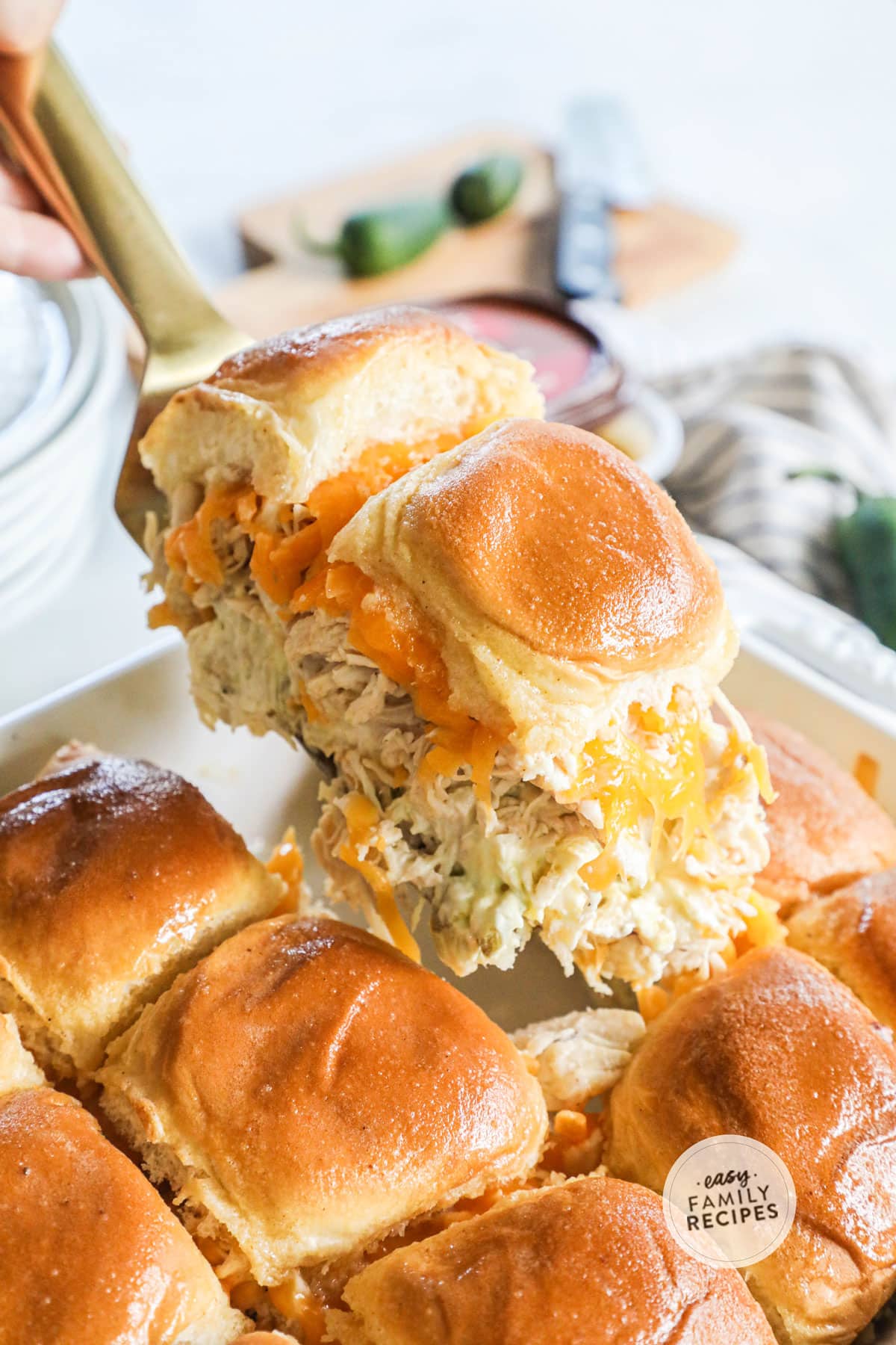 Lifting two jalapeno popper chicken sliders out of the pan to serve