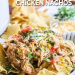 Plate of crockpot chicken nachos topped with cheese, lettuce, pico de gallo, and sour cream