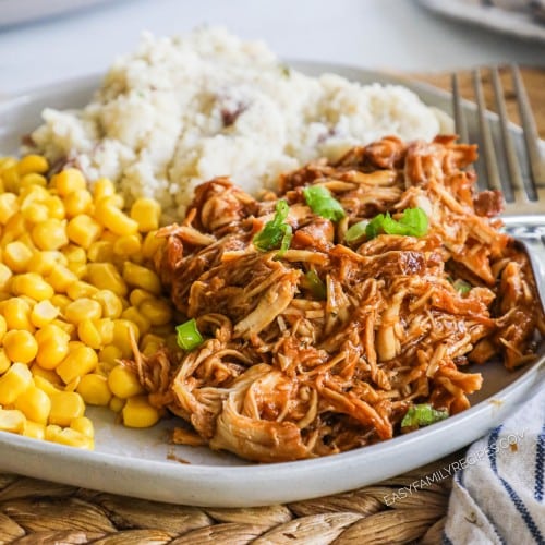 Plate of sauced and shredded chicken on a plate with a side or corn and mashed potatoes.