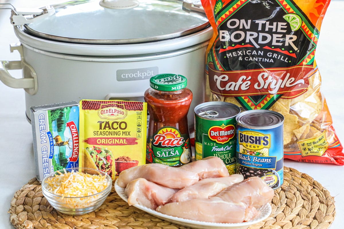 Ingredients for crockpot chicken nachos, including tortilla chips. chicken, cheese, beans, corn, salsa, taco seasoning, and cream cheese