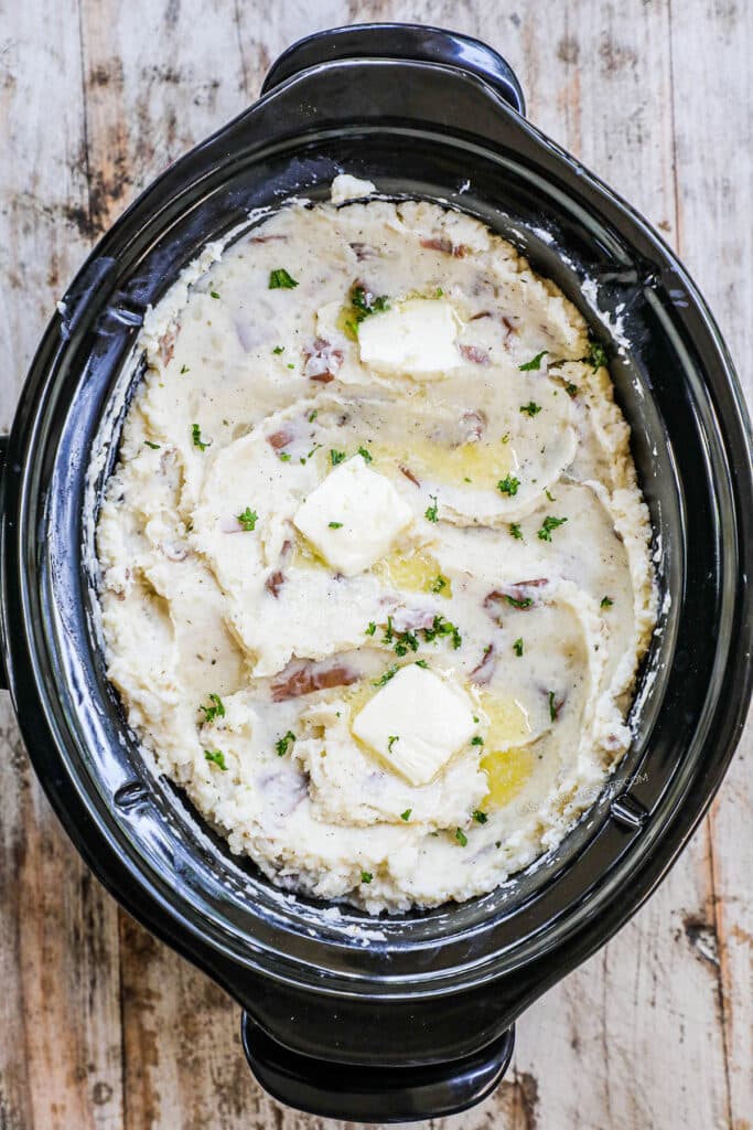 Step 4 - Finished potatoes. Overhead of garlic mashed potatoes in a slow cooker with a spoon.