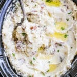 overhead of garlic mashed potatoes in a slow cooker with a spoon.