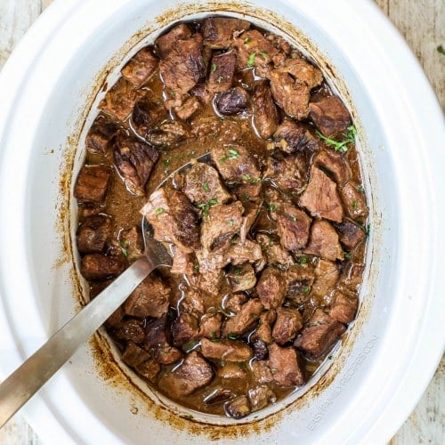 Overhead view of crockpot steak bites in slow cooker with spoon