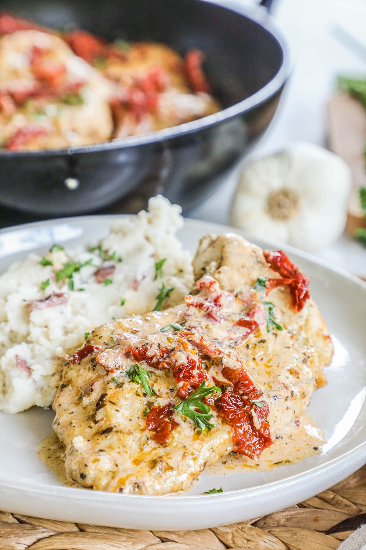 A plate of of marry chicken with a creamy sauce and sun-dried tomatoes and basil next to a side of mashed potatoes