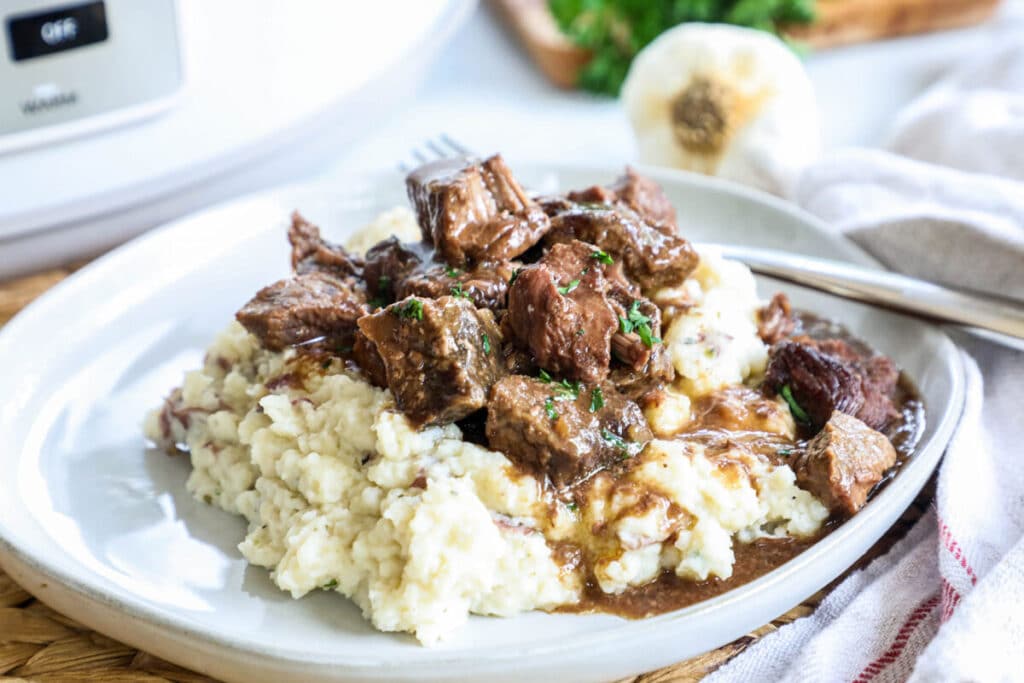 Dinner serving crockpot steak bites with gravy over mashed potatoes.