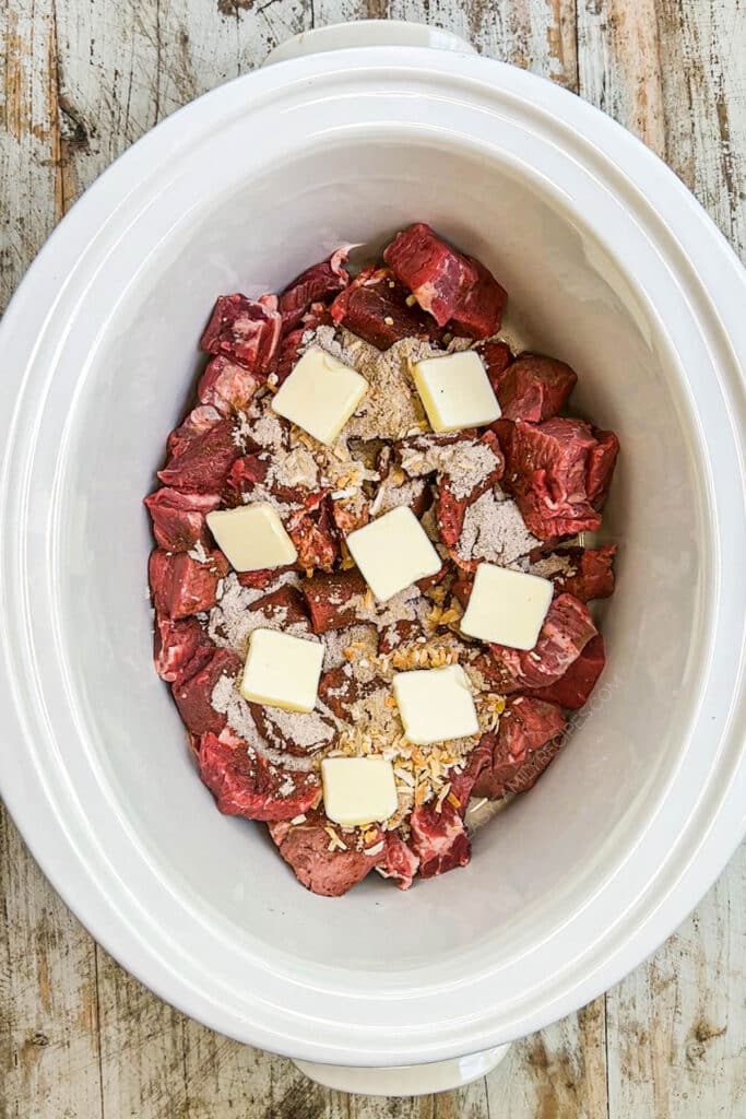 How to make crockpot steak bites step 3: top steak and seasonings with pats of butter.