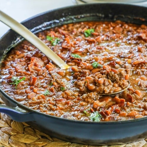Skillet of baked beans with ground beef with serving spoon