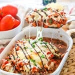 Bruschetta Chicken in a white casserole dish being scooped out