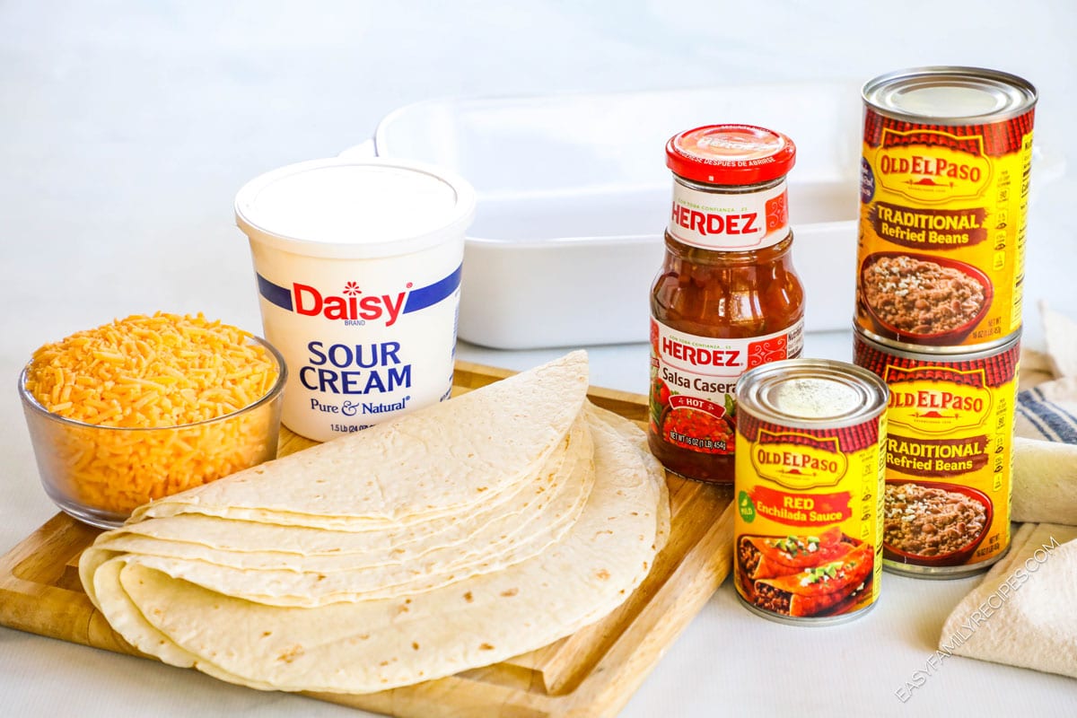 Ingredients for smothered burritos including tortillas, cheese, enchilada sauce, salsa, sour cream, and refried beans.