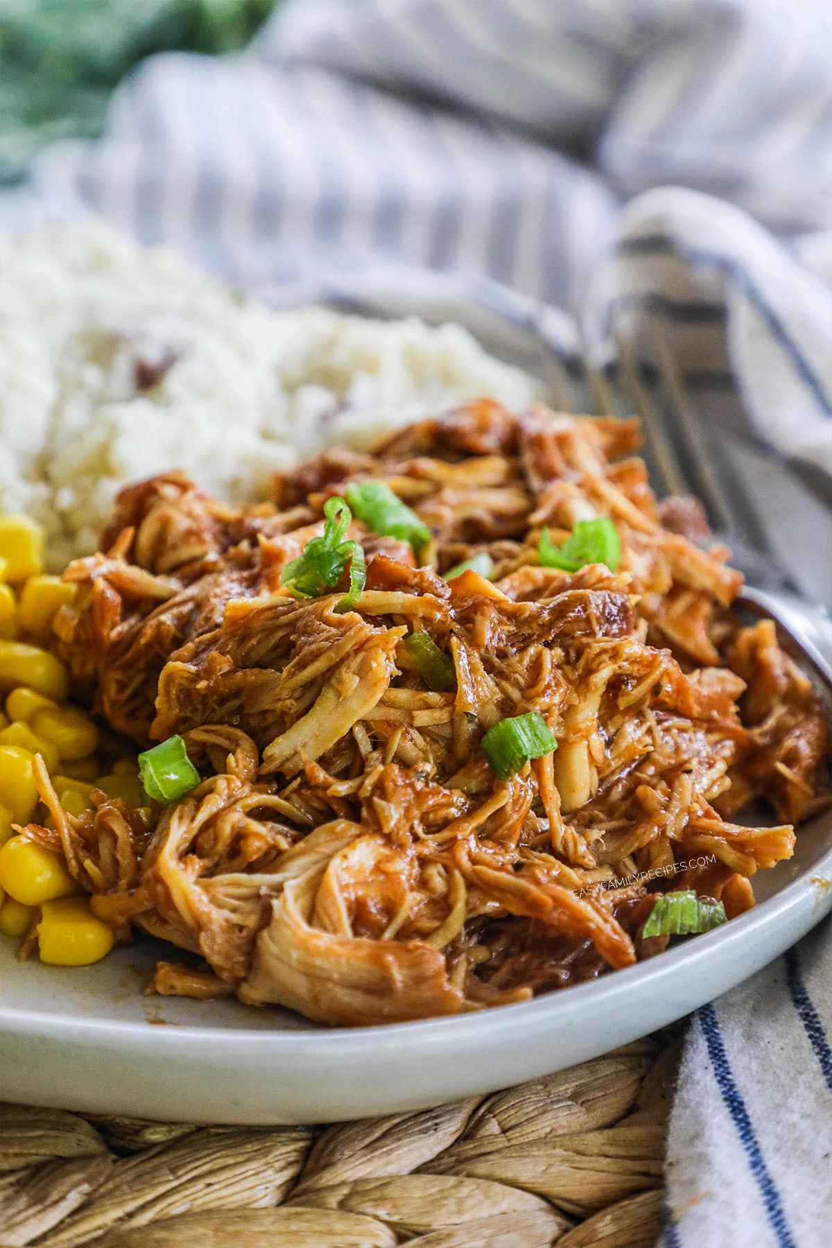 Plate of sauced and shredded chicken on a plate with a side or corn and mashed potatoes.