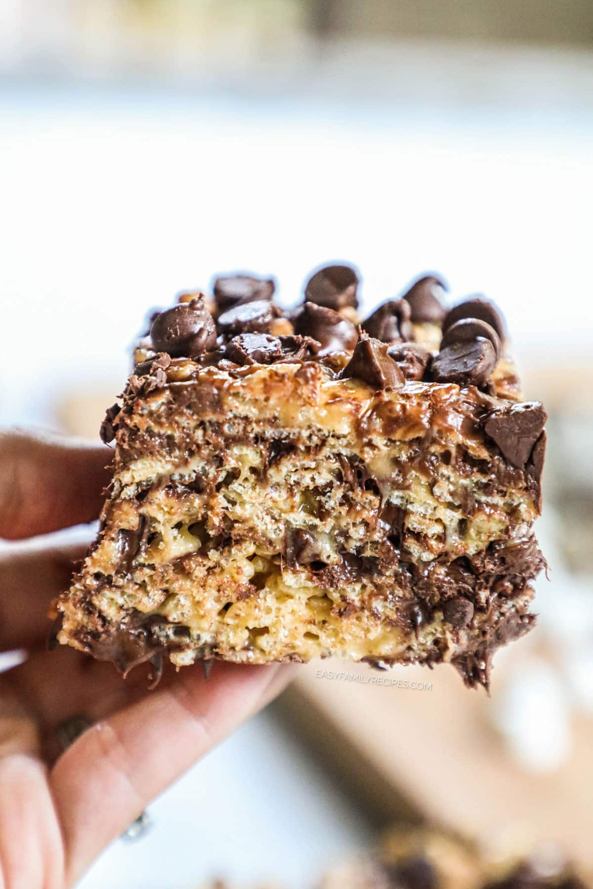 Holding a big, thick peanut butter chocolate rice krispie treat topped with chocolate chips