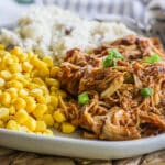 Plate of sauced and shredded chicken on a plate with a side or corn and mashed potatoes.