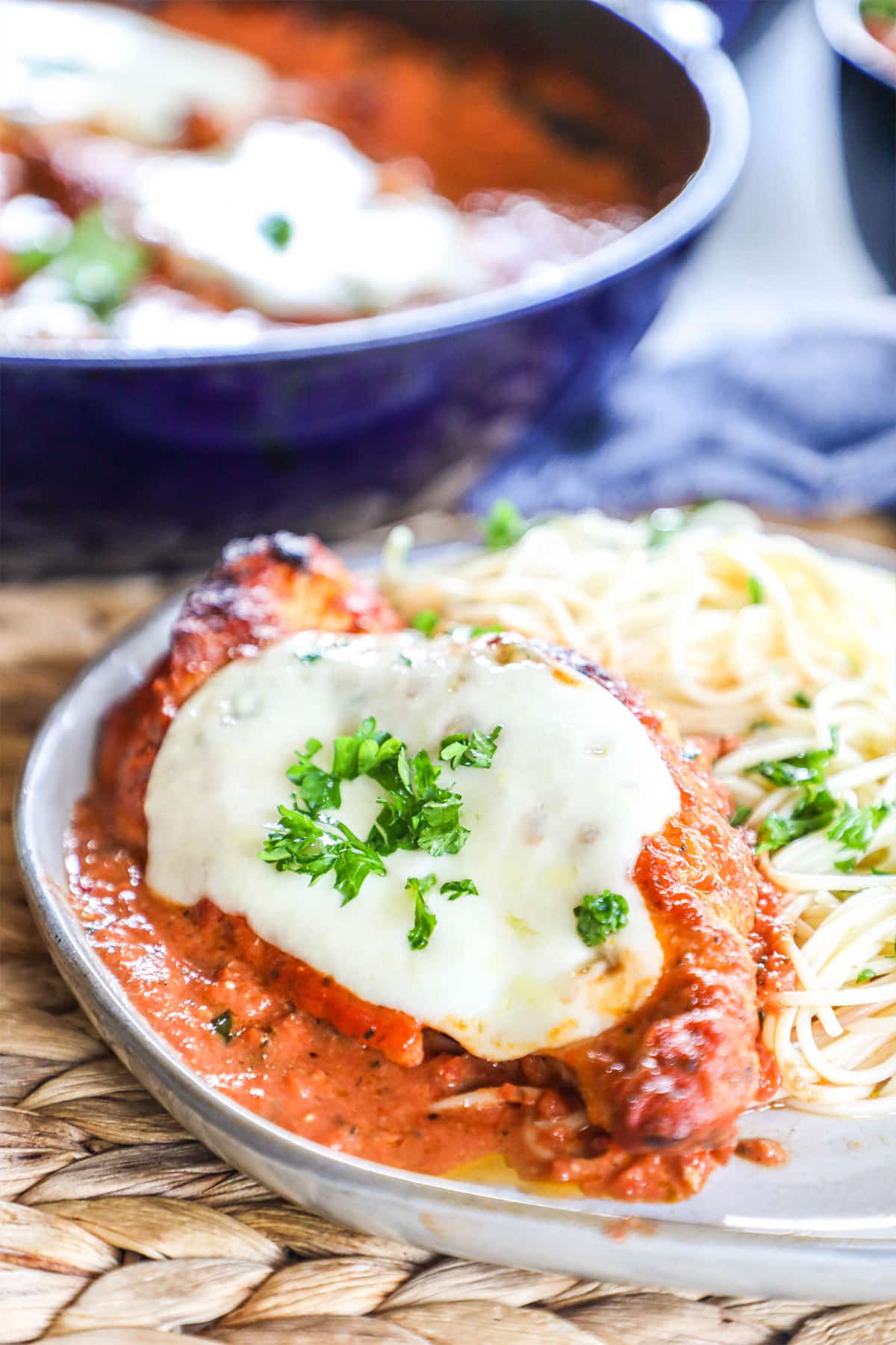 Chicken Mozzarella made in a skillet and plated in creamy tomato sauce topped with basil next to pasta.