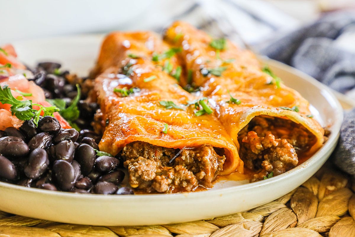 Ground Beef enchiladas served with black beans on a plate.