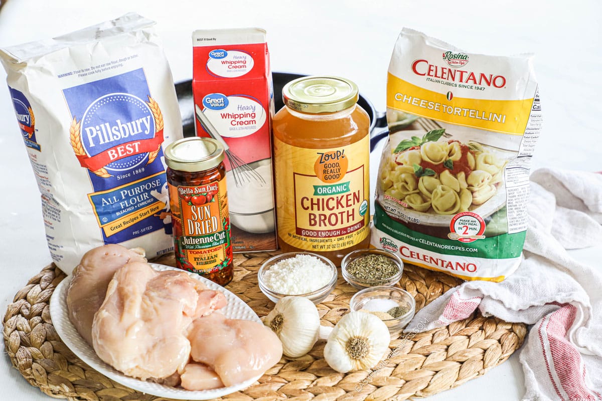 Ingredients for marry me chicken and tortellini, including broth, sun-dried tomatoes, garlic, seasonings, chicken, flour, cream, and tortellini