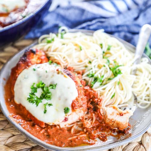 Chicken Mozzarella made in a skillet and plated in creamy tomato sauce topped with basil next to pasta.