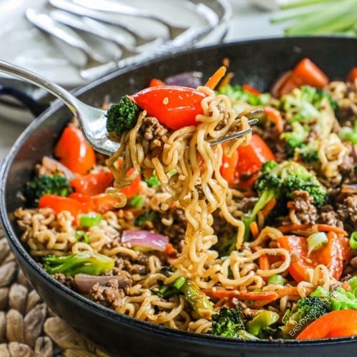 a pan of ground beef and noodle stir fry with red peppers, broccoli, and carrots.