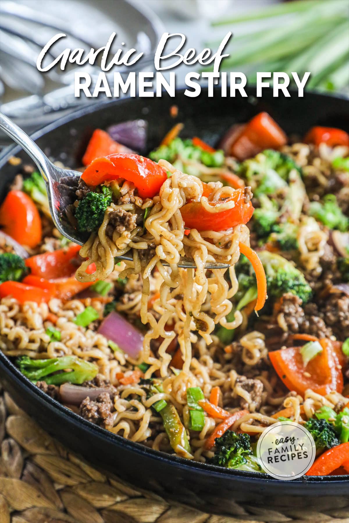 a fork scooping up beef and noodle stir fry with mixed vegetables from a large pan.