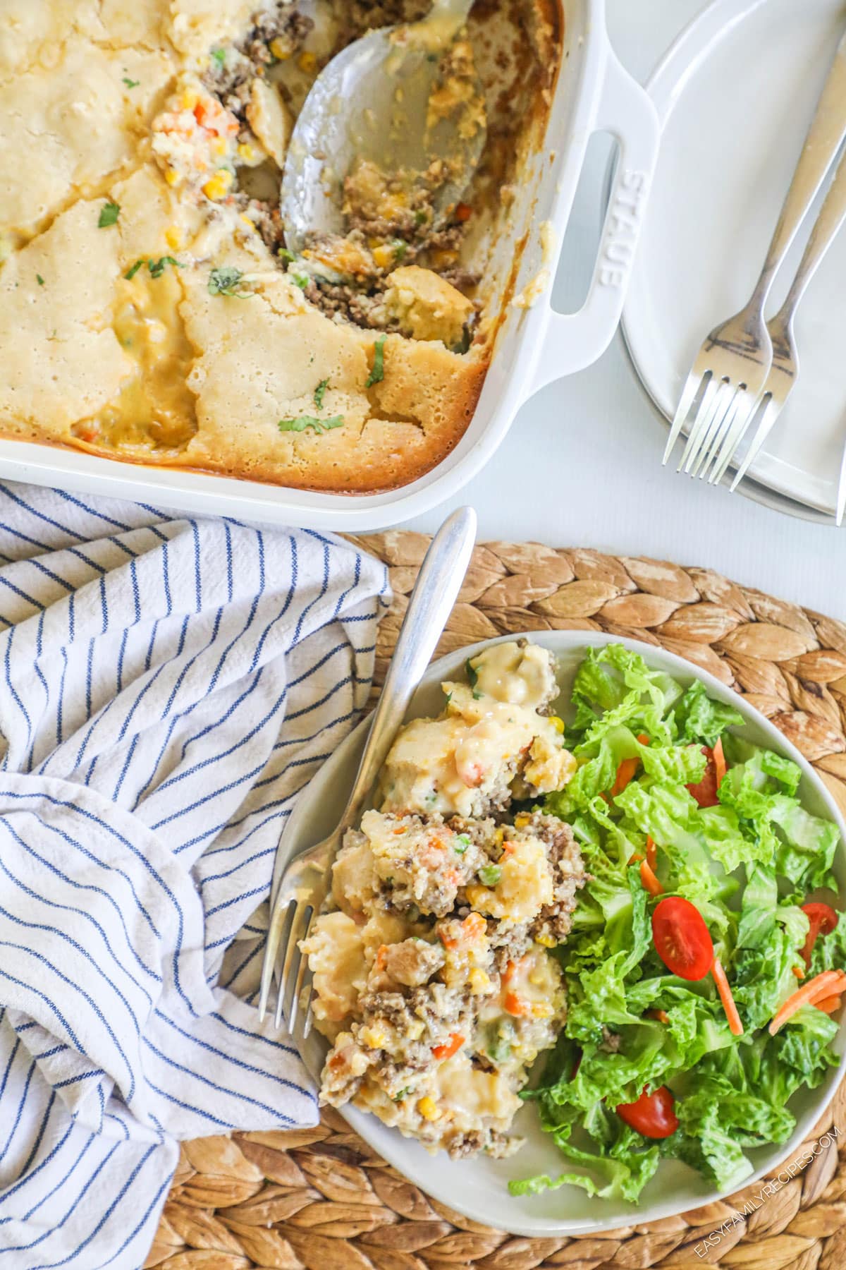 Overhead view of ground beef cobbler on plate with salad with casserole dish of cobbler in background