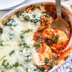 Overhead view of cheese ravioli bake with spinach in casserole dish with serving spoon