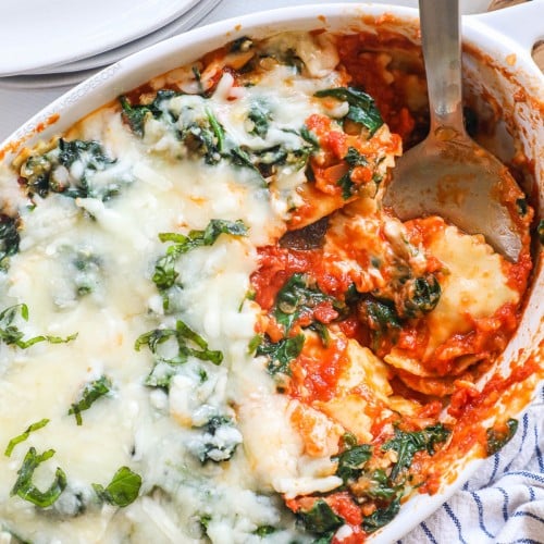 Overhead view of cheese ravioli bake with spinach in casserole dish with serving spoon