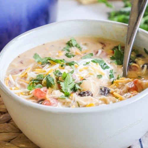 a bowl of creamy chicken tortilla soup with herbs sprinkled on top.