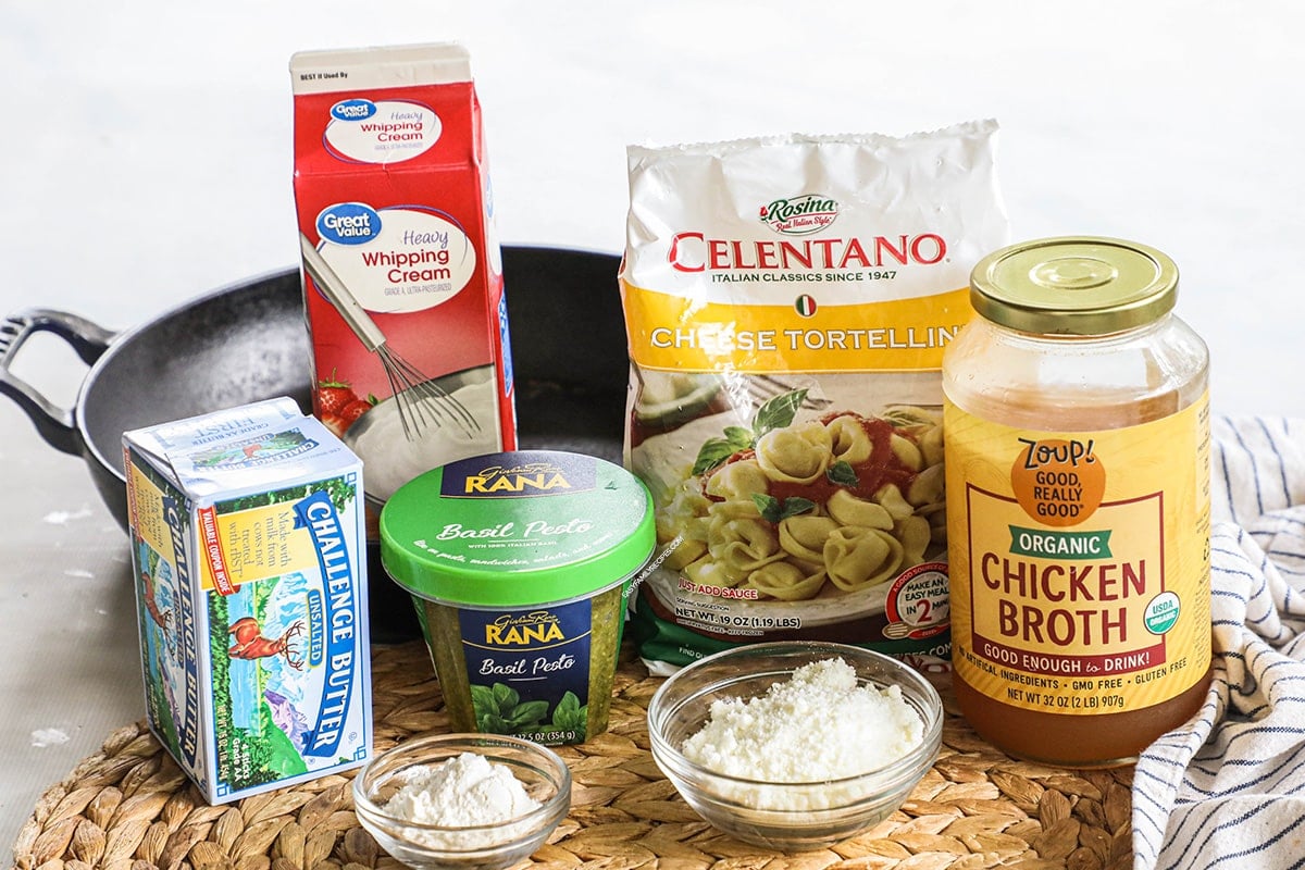 Ingredients to make cheese tortellini with pesto cream sauce including flour, butter, parmesan, pesto, and cream.