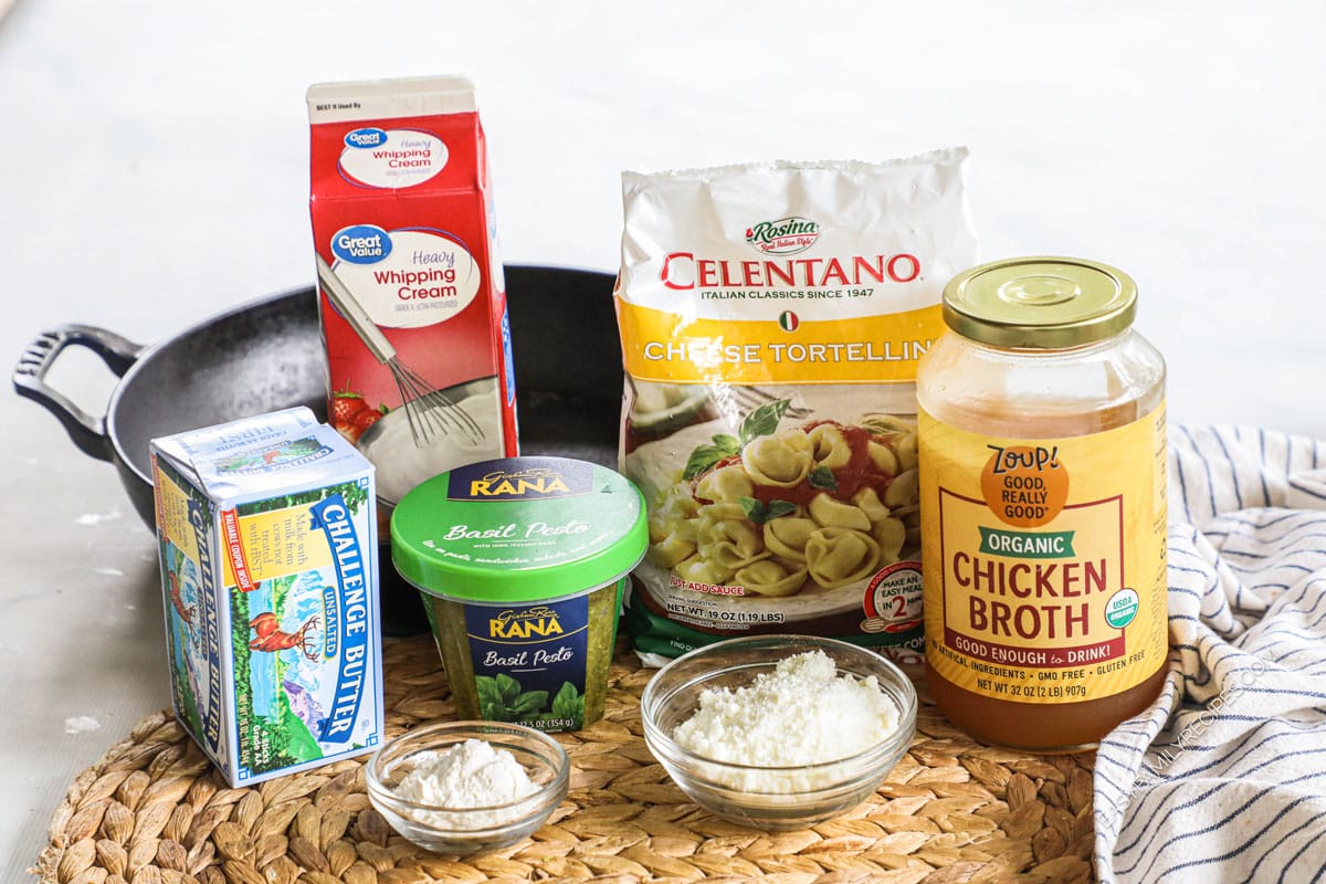 Ingredients to make cheese tortellini with pesto cream sauce including flour, butter, parmesan, pesto, and cream.