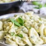 A white plate of tortellini tossed with pesto cream sauce and garnished with fresh basil.