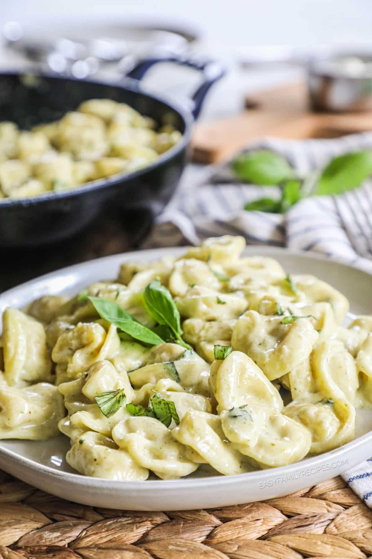 A white plate of tortellini tossed with pesto cream sauce and garnished with fresh basil.