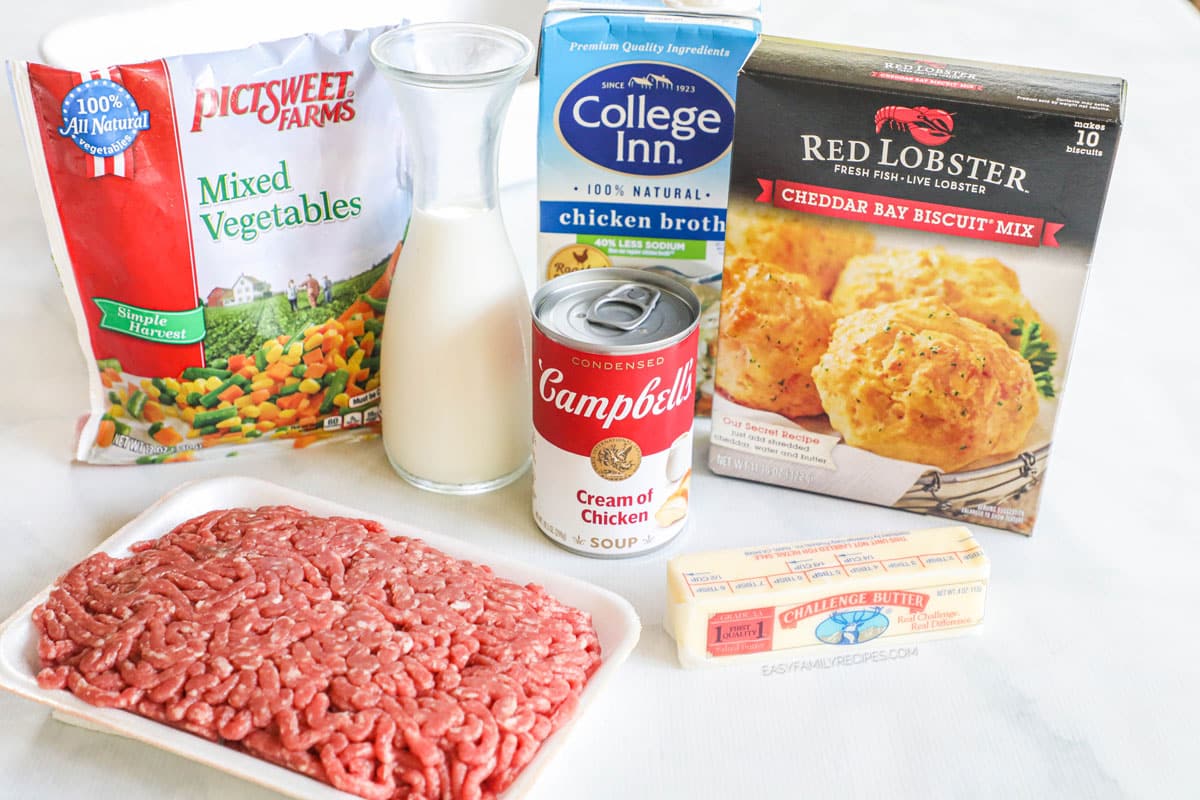 Ingredients for ground beef cobbler, including ground beef, butter, cream of chicken soup, milk, biscuit mix, broth, mixed vegetables